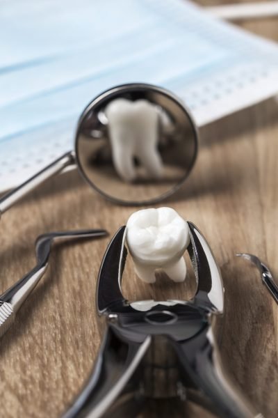 Tooth extraction concept with an array of stainless steel dental tools and a mask with the extracted tooth clasped in the pincers and reflected in the mirror
